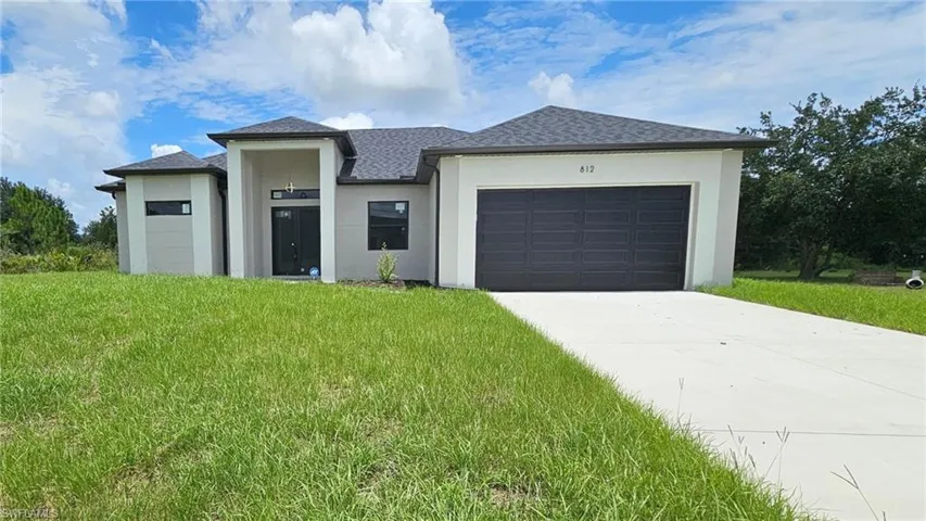 Prairie-style house featuring stucco siding, an attached garage, a front yard, and driveway