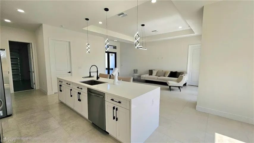Kitchen featuring appliances with stainless steel finishes, open floor plan, a tray ceiling, white cabinetry, and recessed lighting