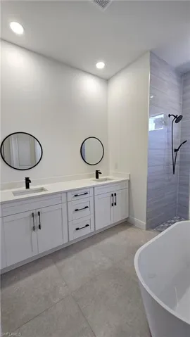 Bathroom with double vanity, a freestanding bath, a tile shower, and recessed lighting
