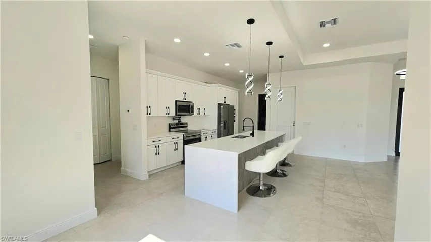 Kitchen featuring an island with sink, stainless steel appliances, a kitchen bar, white cabinets, and hanging light fixtures