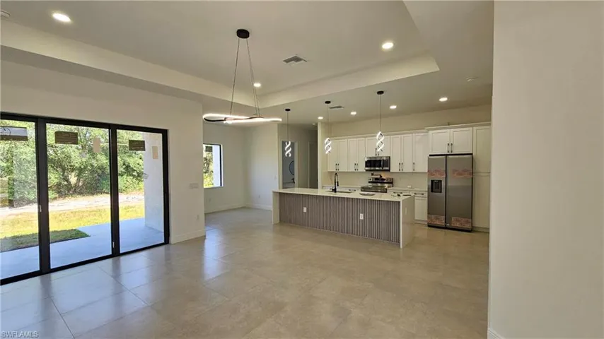 Kitchen featuring stainless steel appliances, recessed lighting, light countertops, white cabinets, and a center island with sink