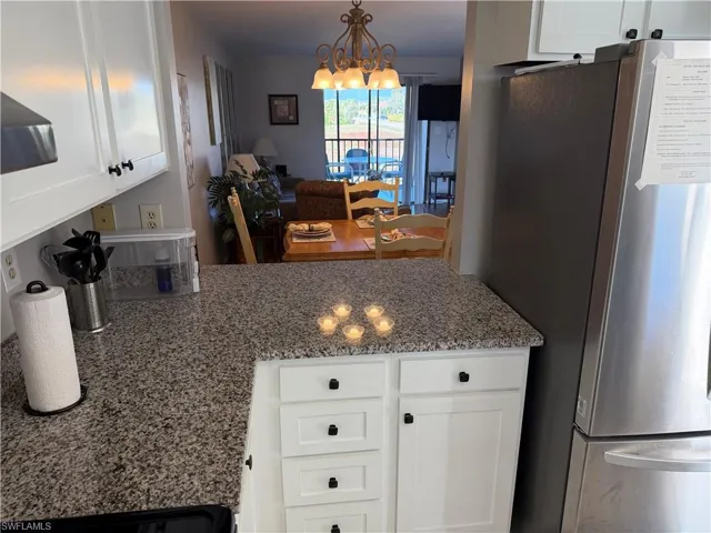 Kitchen featuring white cabinetry, freestanding refrigerator, light stone countertops, and a chandelier