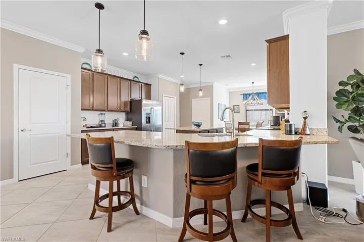 Kitchen with a breakfast bar area, hanging light fixtures, ornamental molding, light stone counters, and brown cabinets