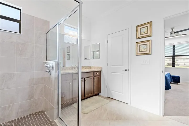 Full bath with vanity, a stall shower, ceiling fan, ornamental molding, and light carpet