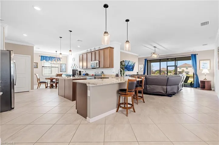 Kitchen featuring crown molding, a peninsula, stainless steel appliances, decorative light fixtures, and a kitchen breakfast bar