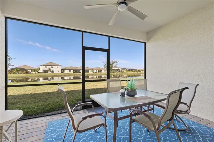 Sunroom / solarium with a textured wall, ceiling fan, outdoor dining space, a residential view, and a water view