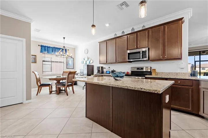 Kitchen with crown molding, decorative light fixtures, dark brown cabinetry, a center island, and light tile patterned floors
