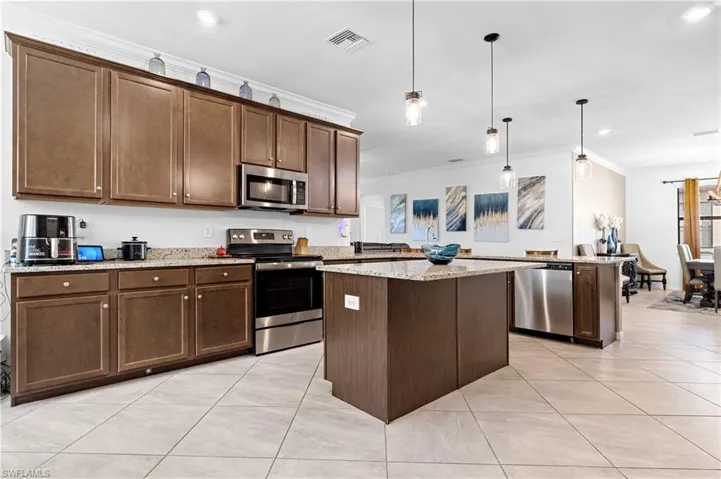 Kitchen with stainless steel appliances, hanging light fixtures, dark brown cabinetry, crown molding, and light tile patterned floors