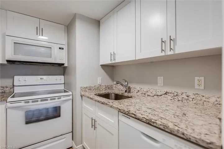 Kitchen featuring white cabinetry, light stone countertops, sink, and white appliances