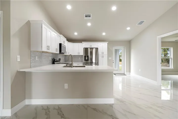 Kitchen featuring lofted ceiling, white cabinets, decorative backsplash, stainless steel appliances, and a peninsula