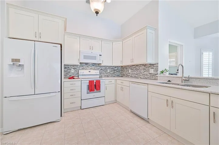 Kitchen featuring white cabinets, backsplash, light tile patterned floors, white appliances, and sink