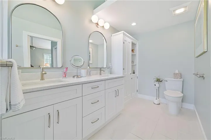 Bathroom with tile flooring, double sink, large vanity, ceiling fan, and toilet