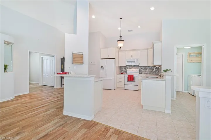 Kitchen featuring white appliances, washing machine and clothes dryer, a center island, hanging light fixtures, and light hardwood / wood-style floors