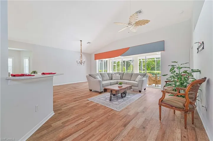 Living room featuring ceiling fan with notable chandelier, light hardwood / wood-style floors, and vaulted ceiling