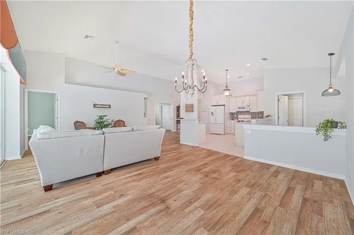 Living room featuring light wood-type flooring, ceiling fan with notable chandelier, and high vaulted ceiling