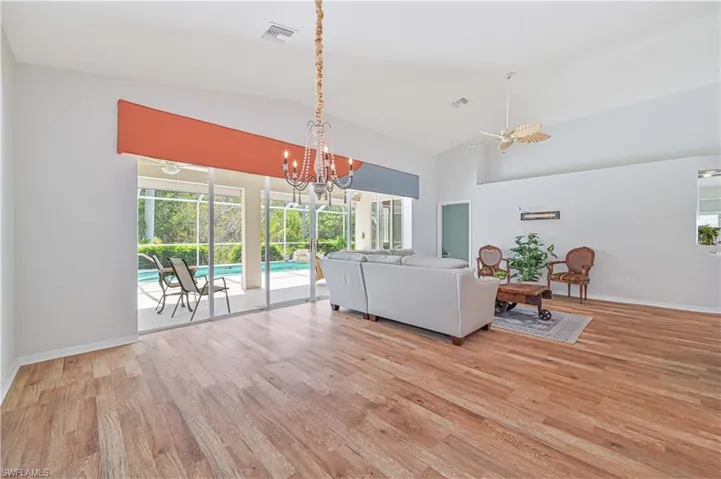 Living room with ceiling fan with notable chandelier, vaulted ceiling, and light hardwood / wood-style floors