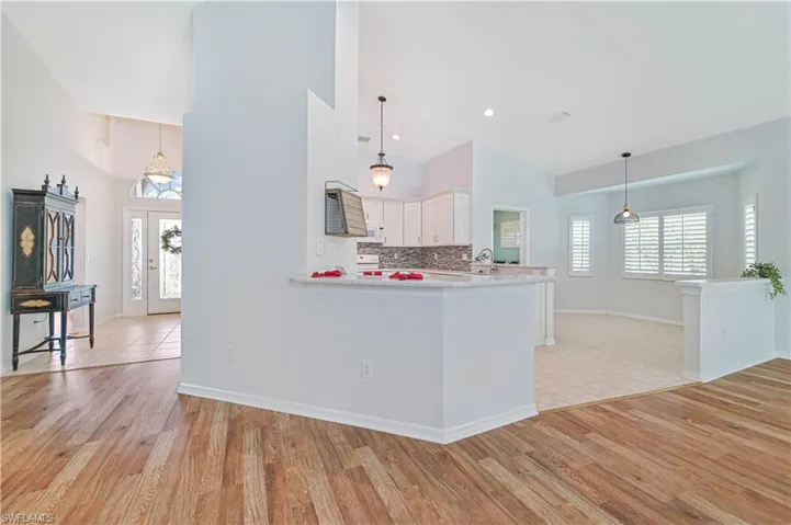 Kitchen featuring light hardwood / wood-style floors, white cabinetry, kitchen peninsula, high vaulted ceiling, and pendant lighting