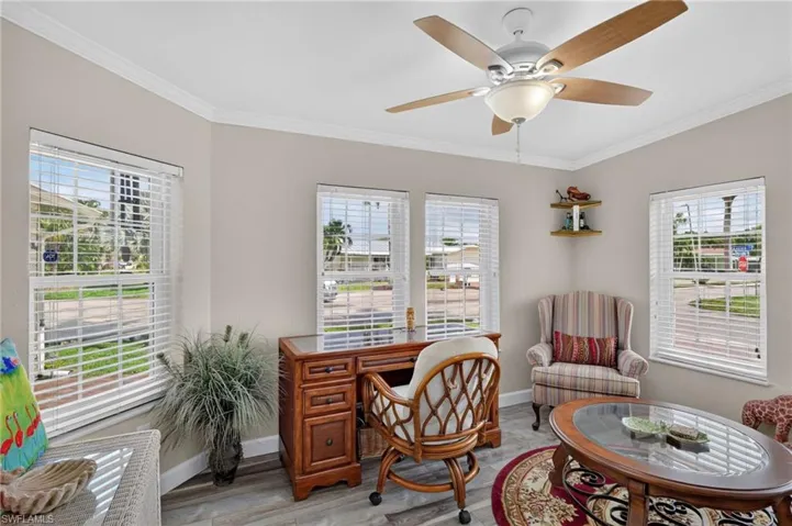 Multiple windows with blinds, wood-finish flooring, ceiling fan with light fixture, and crown molding