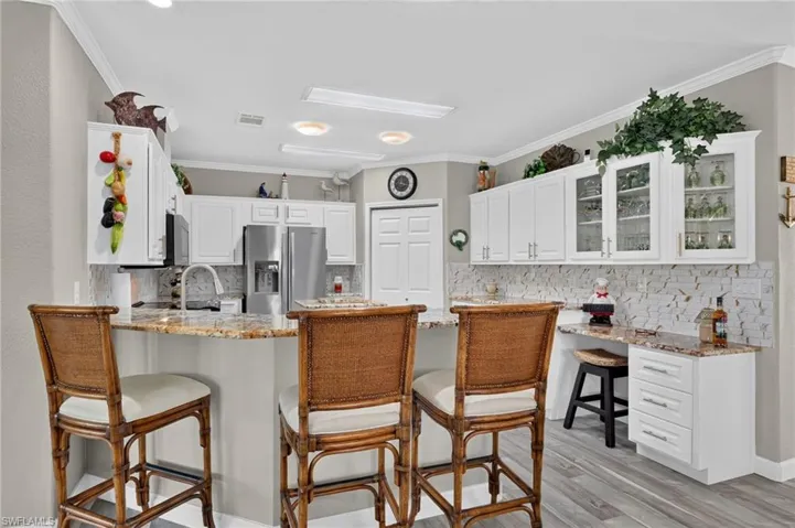 Kitchen featuring white cabinetry, granite countertops, stainless steel appliances, a tile backsplash, and wood-finish flooring