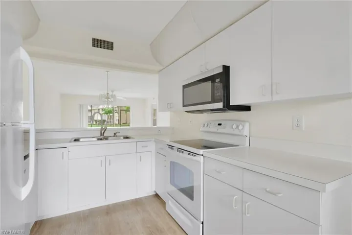 Kitchen with white appliances, light countertops, white cabinets, and light wood-type flooring