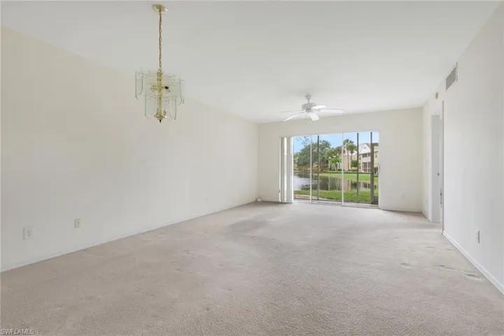 Carpeted empty room with ceiling fan, a chandelier, and a water view