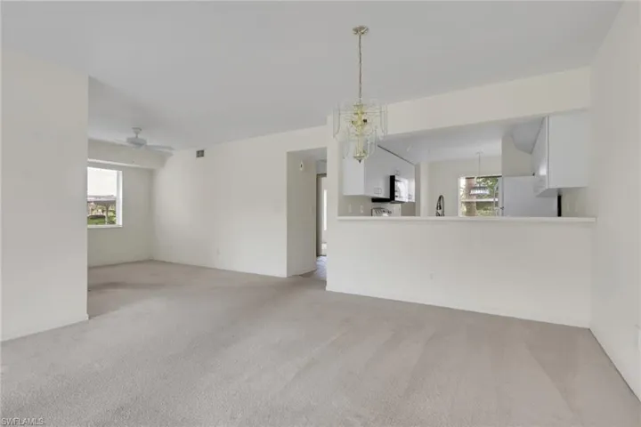 Unfurnished living room featuring light carpet, ceiling fan, and a chandelier
