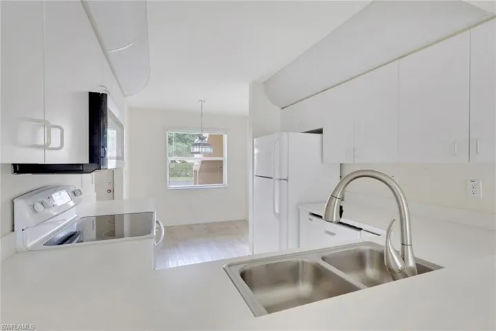 Kitchen featuring light countertops, hanging light fixtures, white appliances, white cabinetry, and light wood-style floors