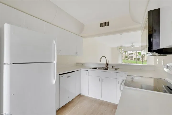 Kitchen featuring white appliances, white cabinets, light countertops, and light wood-style flooring