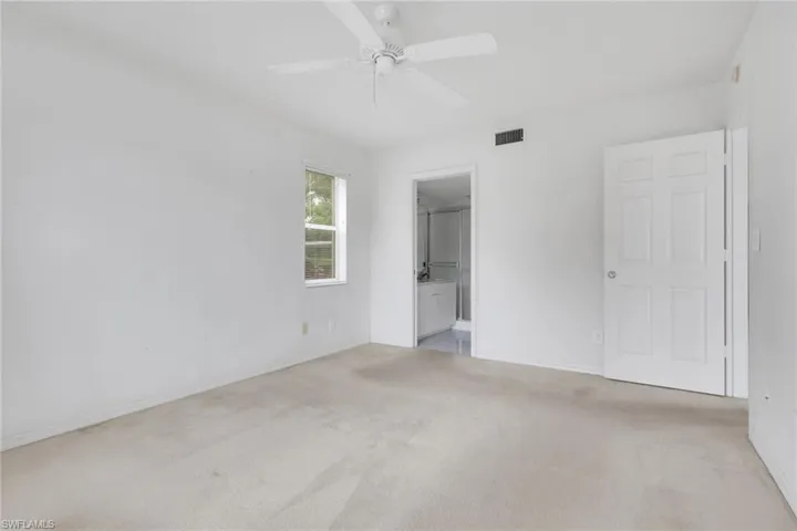Unfurnished bedroom with light colored carpet, ensuite bath, and ceiling fan