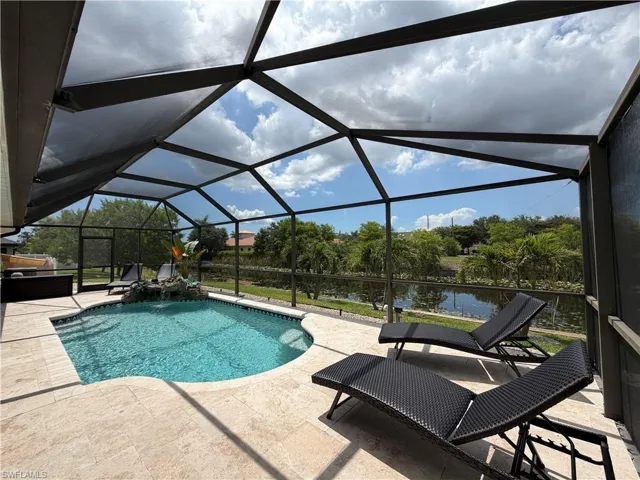 Screened lanai featuring a freeform swimming pool with a rock waterfall detail, surrounded travertine paver decking