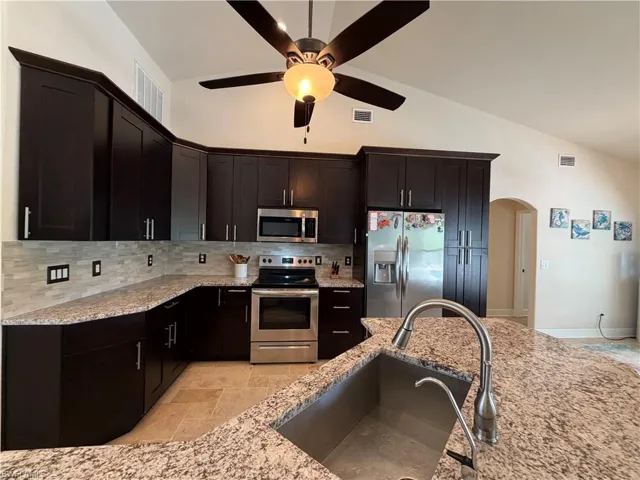 Kitchen featuring dark wood cabinetry with crown molding, stainless steel appliances, granite countertops, and a tile backsplash