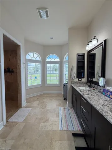 Primary Bathroom featuring a dual vanity with a granite countertops, a large framed mirror, and three arched windows with plantation shutters