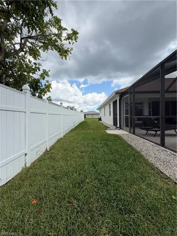 Private side yard space featuring a white privacy fence, screened lanai, and a gravel perimeter alongside the home