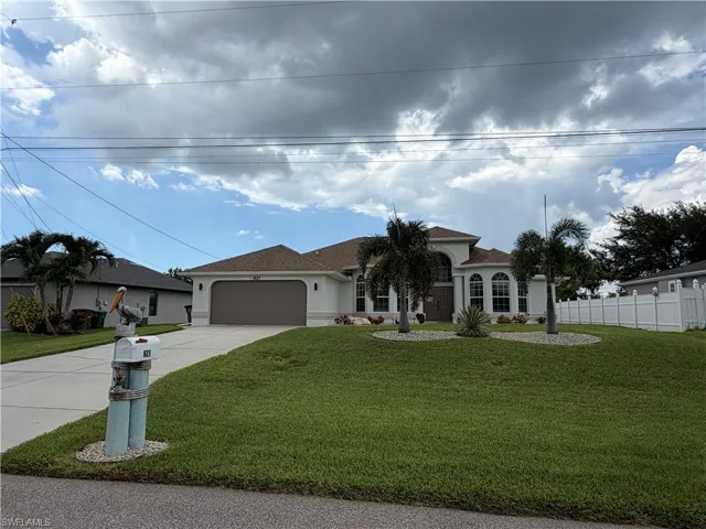 Upscaled landscaping, Stucco exterior with a brown tile roof, mature palm trees, arched windows, an attached garage, and a white privacy fence