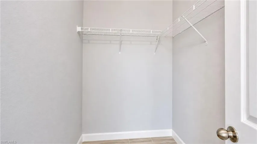 Walk-in closet with wire shelving system, light gray wall finish, white baseboards, and wood-finish tile flooring