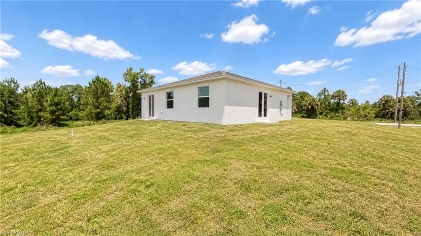 Expansive green lawn surrounds a white stucco property with multiple windows and doors