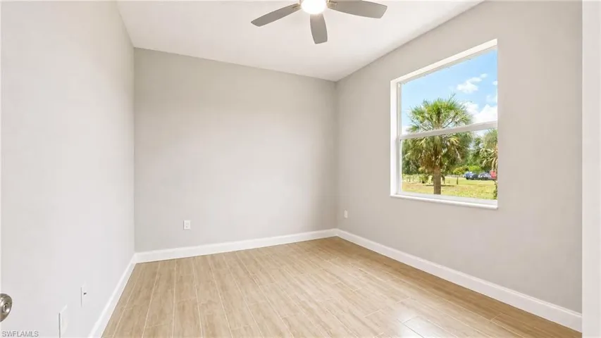 Neutral-toned room featuring wood-finish flooring, a ceiling fan, and a large window with white trim