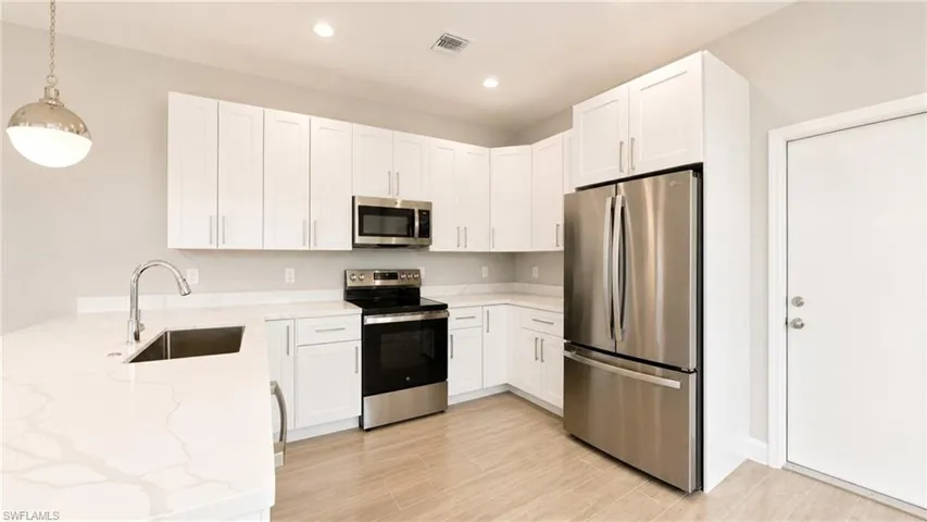 Modern kitchen featuring white shaker cabinetry, stainless steel appliances, light-toned countertops, a stainless steel sink with a high-arch faucet, and wood-finish flooring