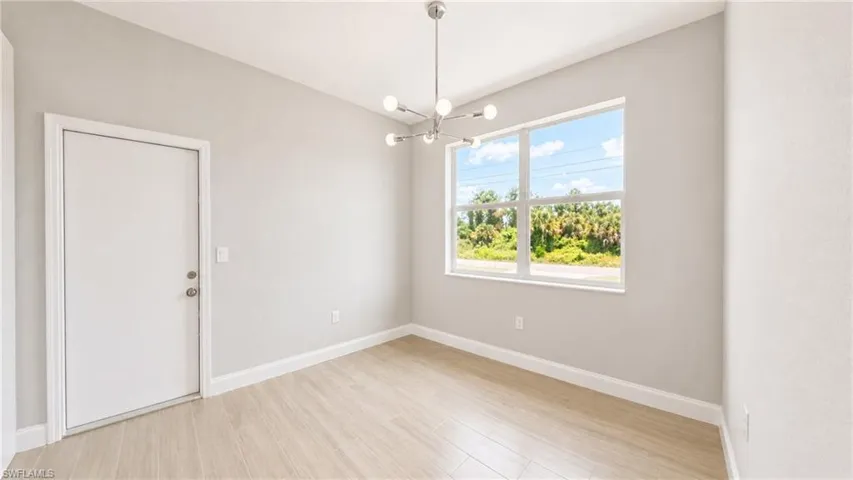 Open room featuring a multi-pane window, wood-finish flooring, a contemporary chandelier, and a white interior door