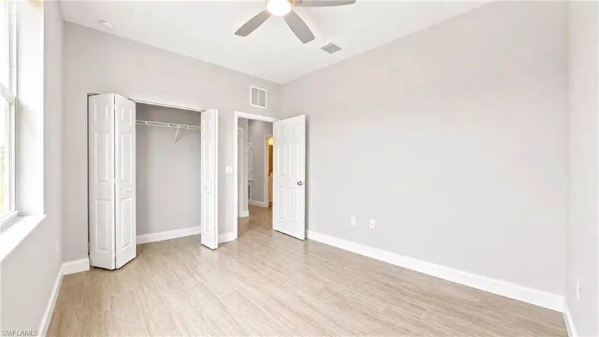 Light-filled room featuring wood-finish flooring, a ceiling fan, white bi-fold closet doors, and white baseboards