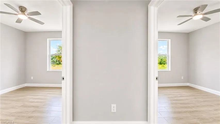 Bright interior room featuring wood-finish tile flooring, a window with natural scenery, a ceiling fan with integrated lighting, and white baseboards