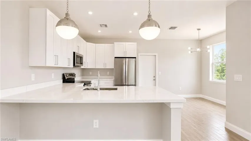 Modern kitchen featuring white cabinetry, stainless steel appliances, quartz countertops, a dual basin undermount sink, and recessed lighting