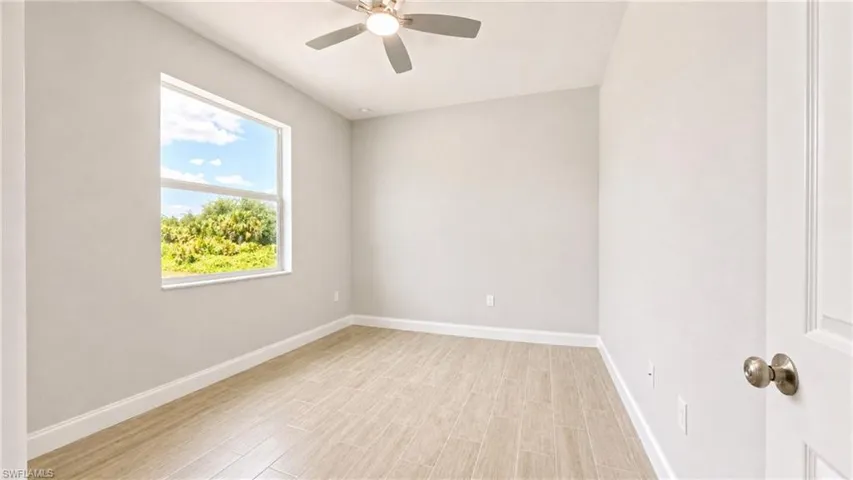 Bright interior space featuring a window with natural scenery, wood-finish flooring, a ceiling fan, and white baseboards