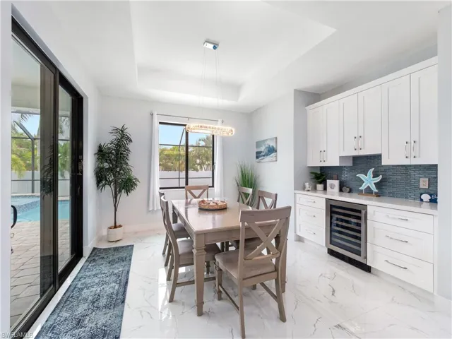 Dining area featuring beverage cooler, a raised ceiling, a chandelier, and light marble finish flooring