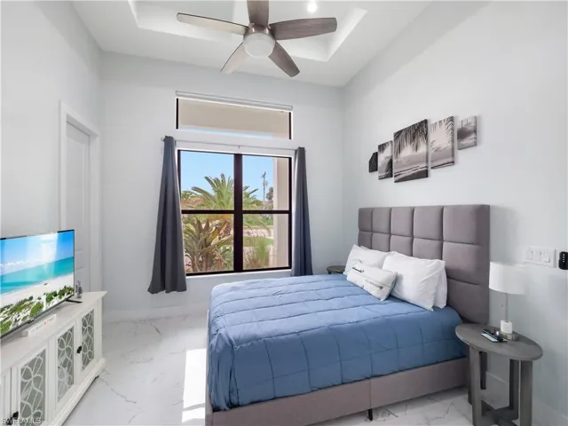 Bedroom featuring light marble finish flooring, a ceiling fan, and a tray ceiling