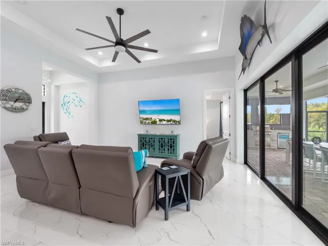 Living area featuring a ceiling fan, a raised ceiling, beverage cooler, recessed lighting, and light marble finish flooring