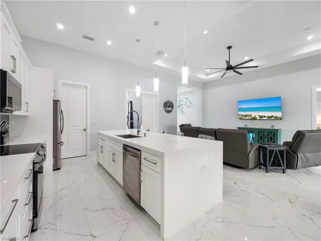 Kitchen featuring white cabinets, open floor plan, a kitchen island with sink, hanging light fixtures, and a tray ceiling