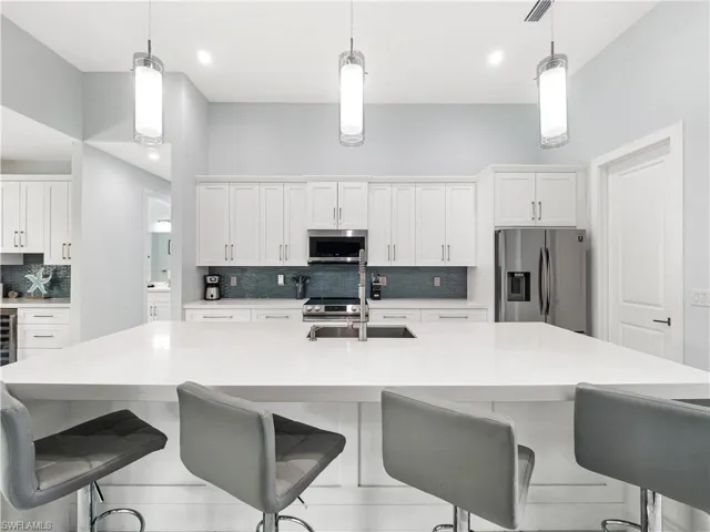 Kitchen featuring decorative backsplash, a kitchen breakfast bar, stainless steel appliances, and white cabinets
