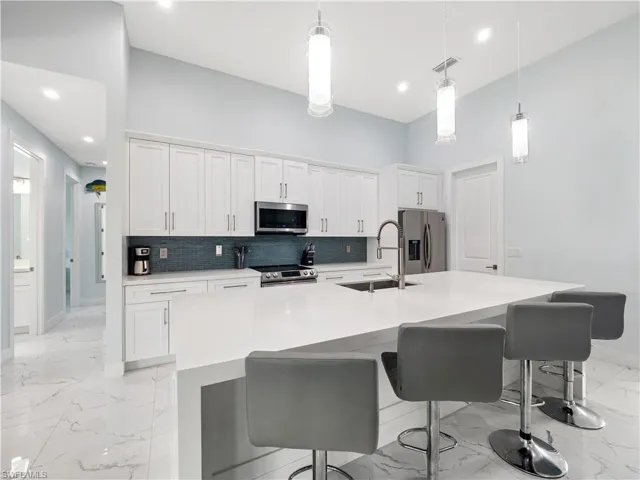 Kitchen featuring light marble finish floors, white cabinets, stainless steel appliances, a kitchen island with sink, and light stone counters