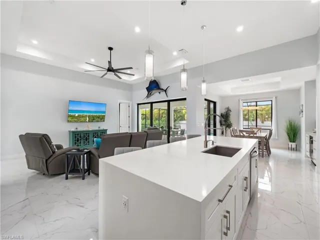 Kitchen featuring a raised ceiling, open floor plan, an island with sink, light stone counters, and hanging light fixtures
